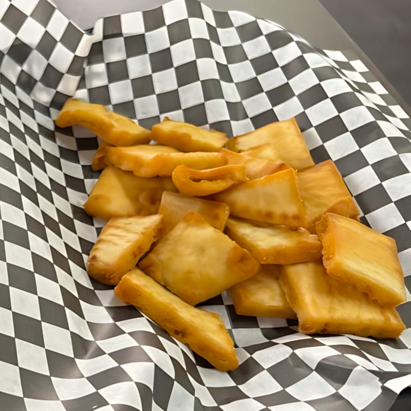 Golden brown fried yucca fries served in a black and white checkered paper basket.