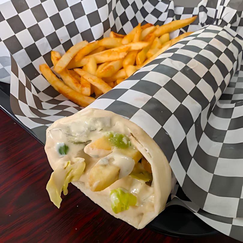 A Sandwich Planet wrap with creamy sauce and fries in checkered paper on a dark tray.