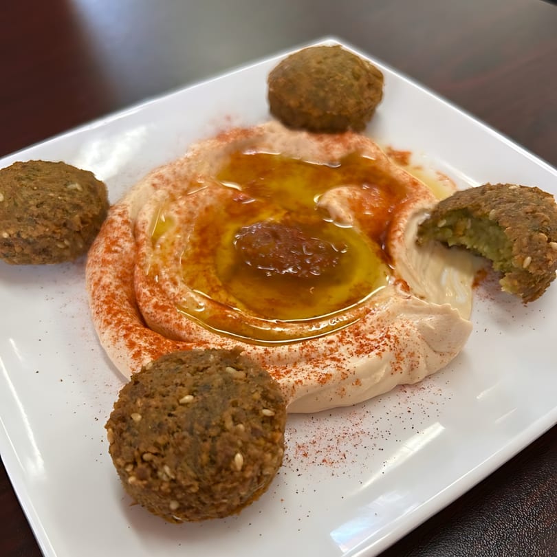 A white plate with hummus drizzled with olive oil and paprika, surrounded by four falafel.
