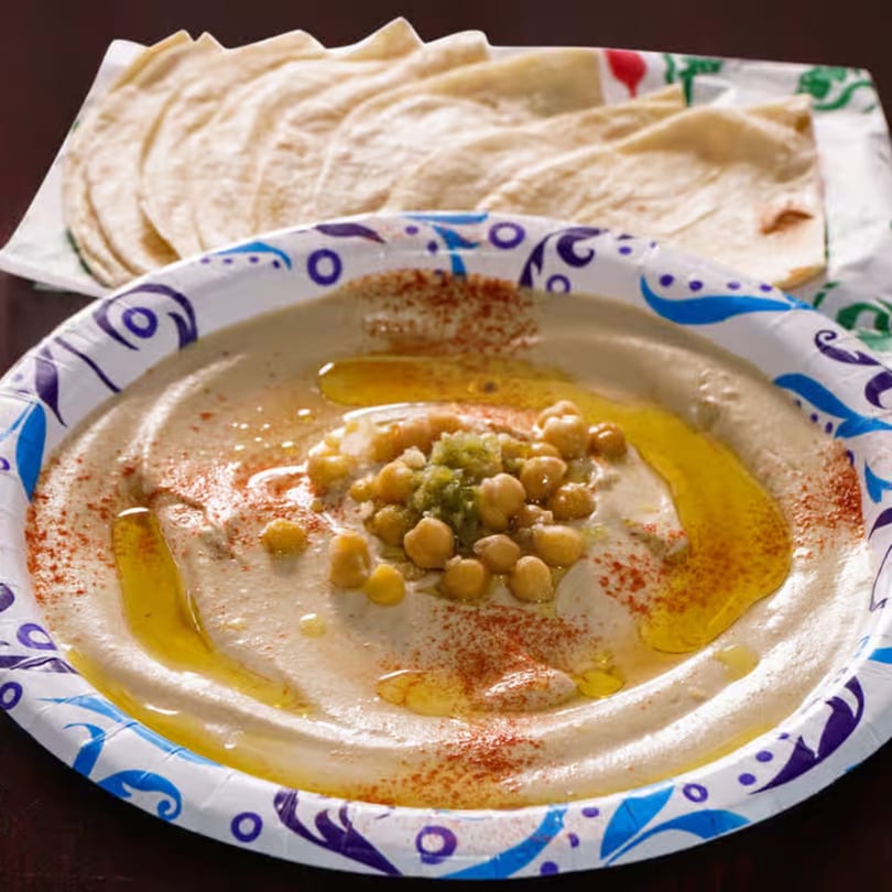 Hummus topped with chickpeas, olive oil, and paprika, served with pita bread.