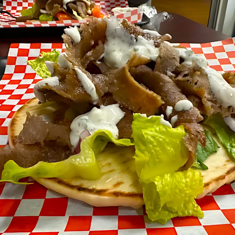 Gyro sandwich with sliced meat, lettuce, and white sauce on pita bread, on a red and white checkered paper.