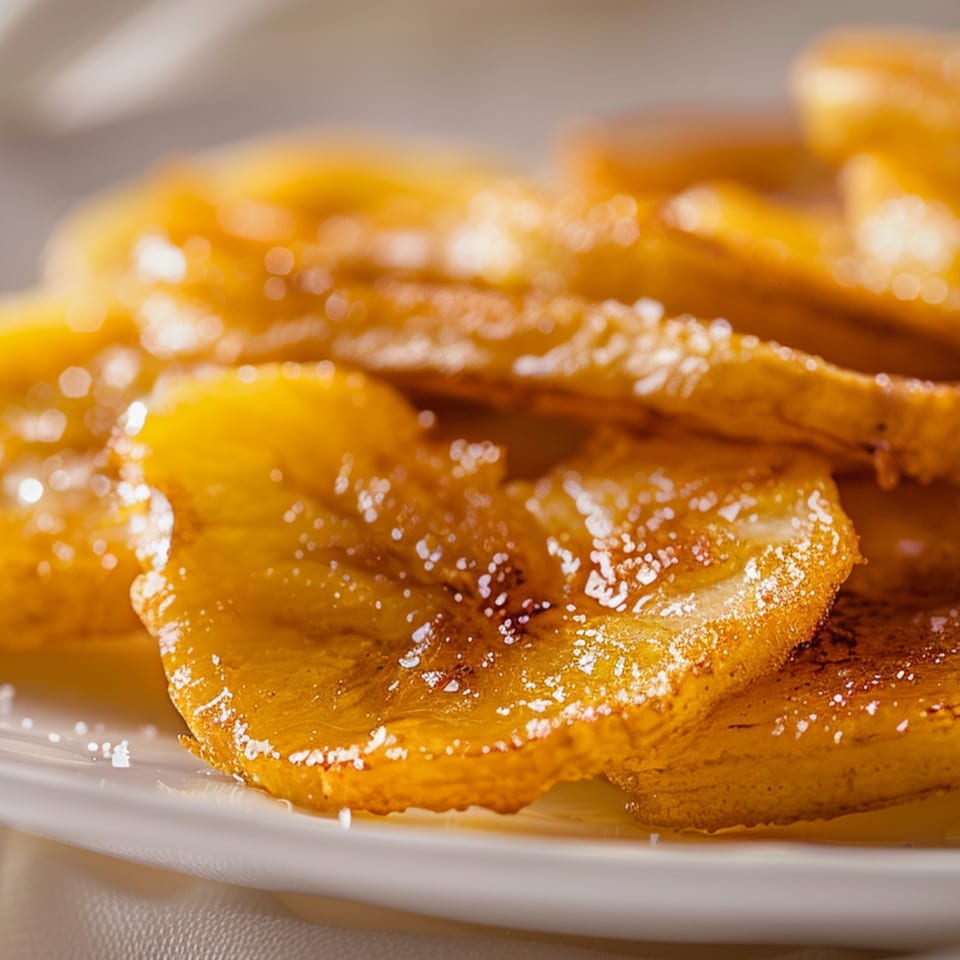 Close-up of golden-brown fried banana slices dusted with powdered sugar on a white plate.