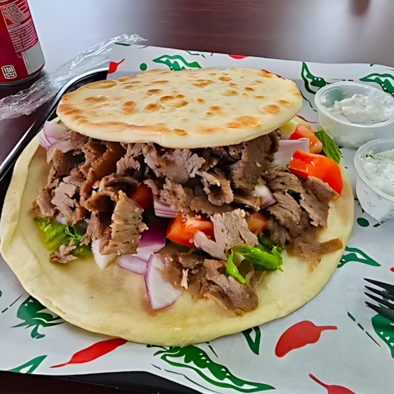A large gyro sandwich with meat, lettuce, tomatoes, and onions on pita bread.